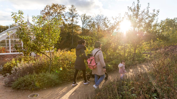 Visitors walking along a path near the small glass house in the upper garden